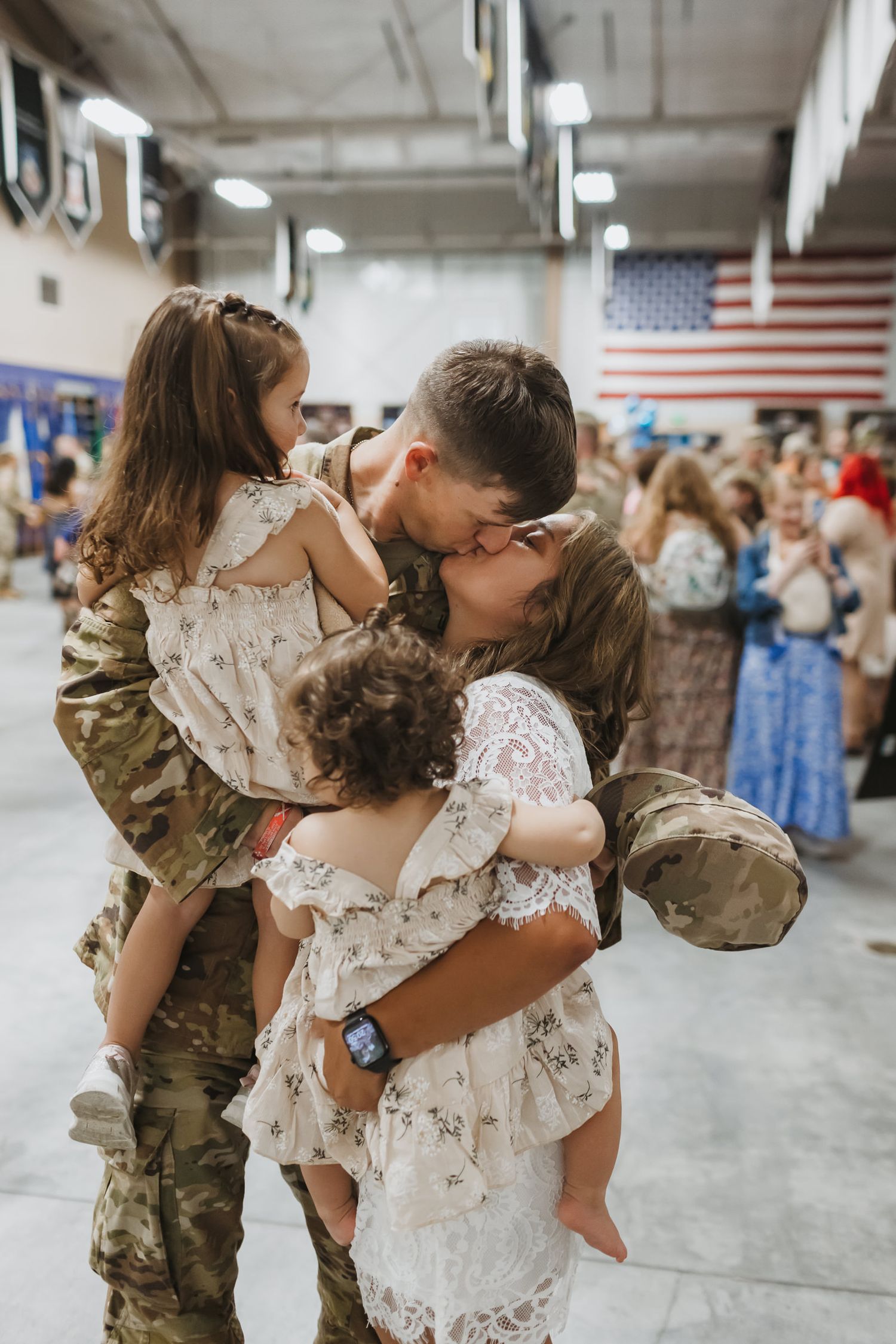 soldier kissing his wife while holding his toddler daughter after returning home from deployment overland park photographer