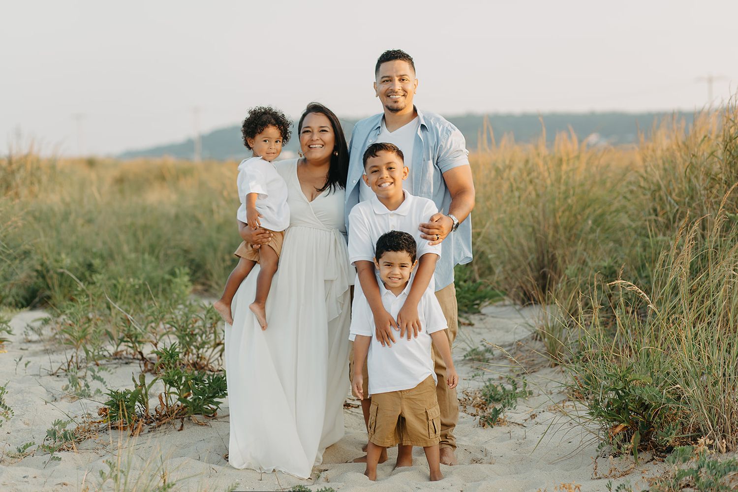 A family wearing white outfits poses together on a sandy beach during golden hour.