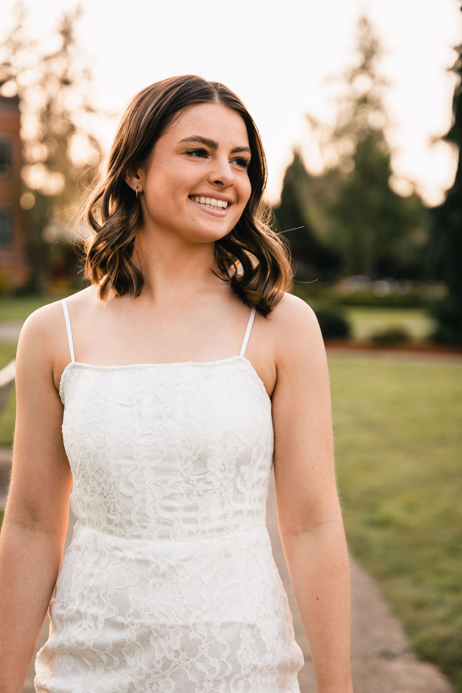 A woman in a white dress smiling outdoors during golden hour for a portrait photo shoot.