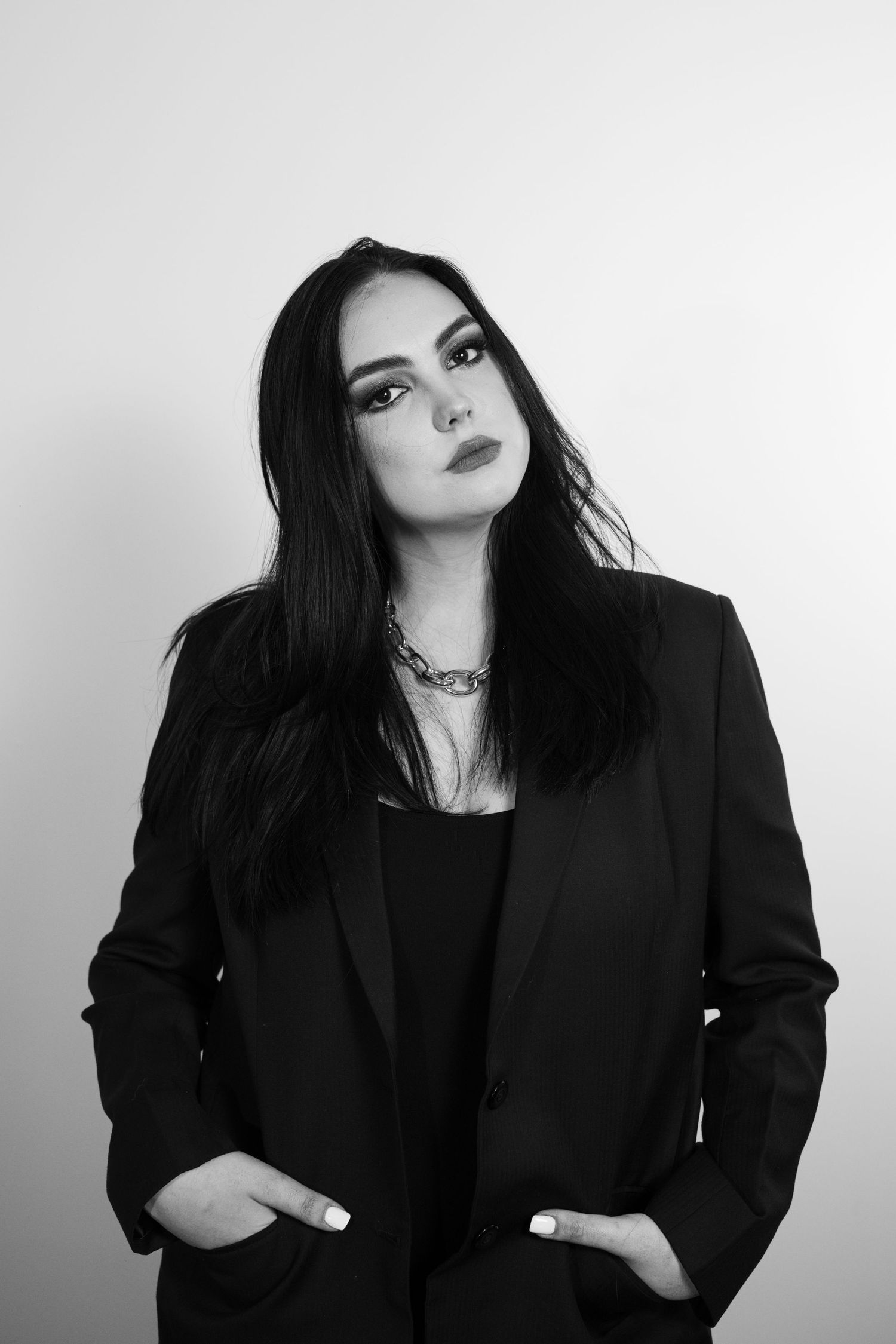 Black and white portrait of someone in dark blazer with bold makeup against white background.