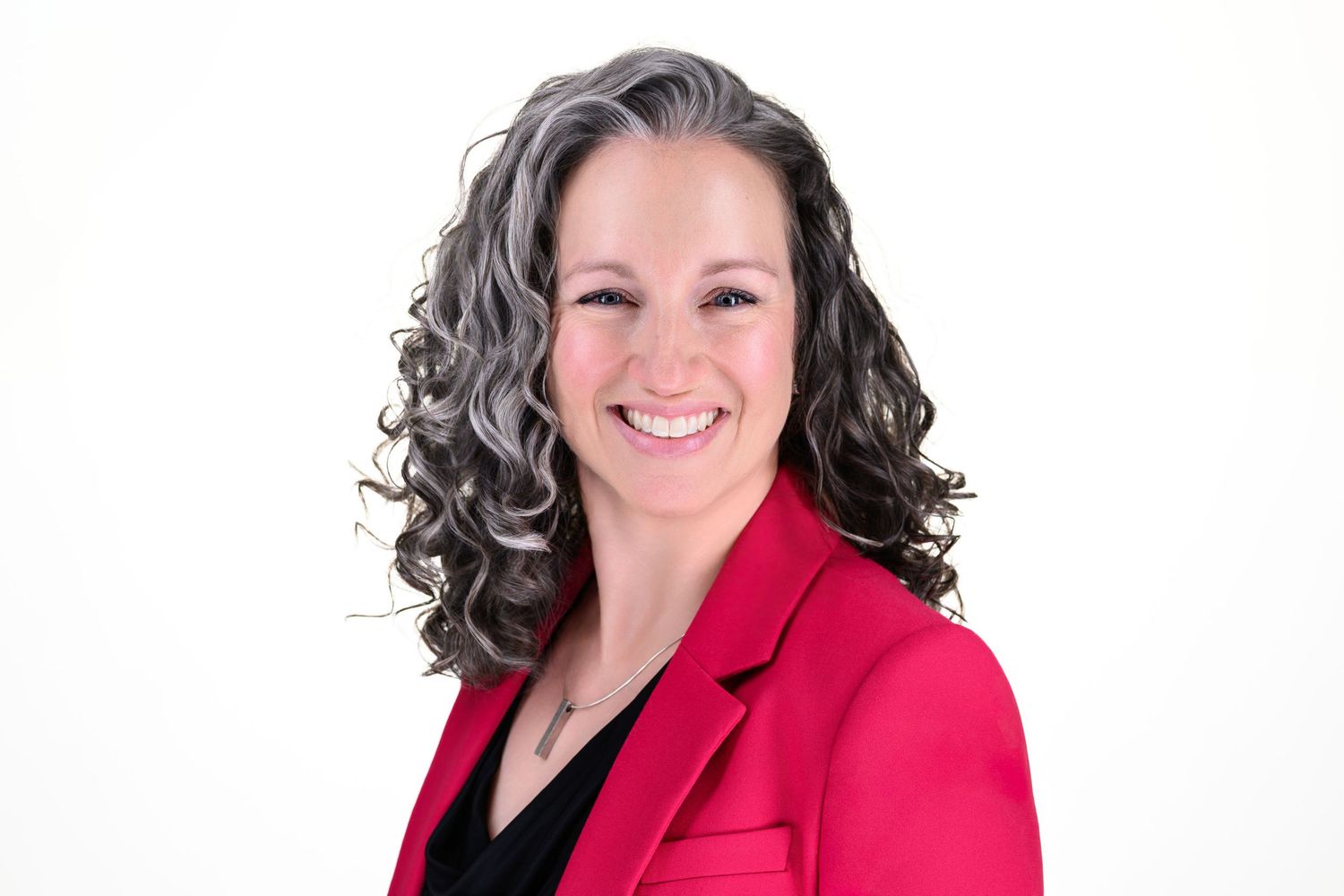 Professional headshot against black background featuring someone in a red top with curly hair.
