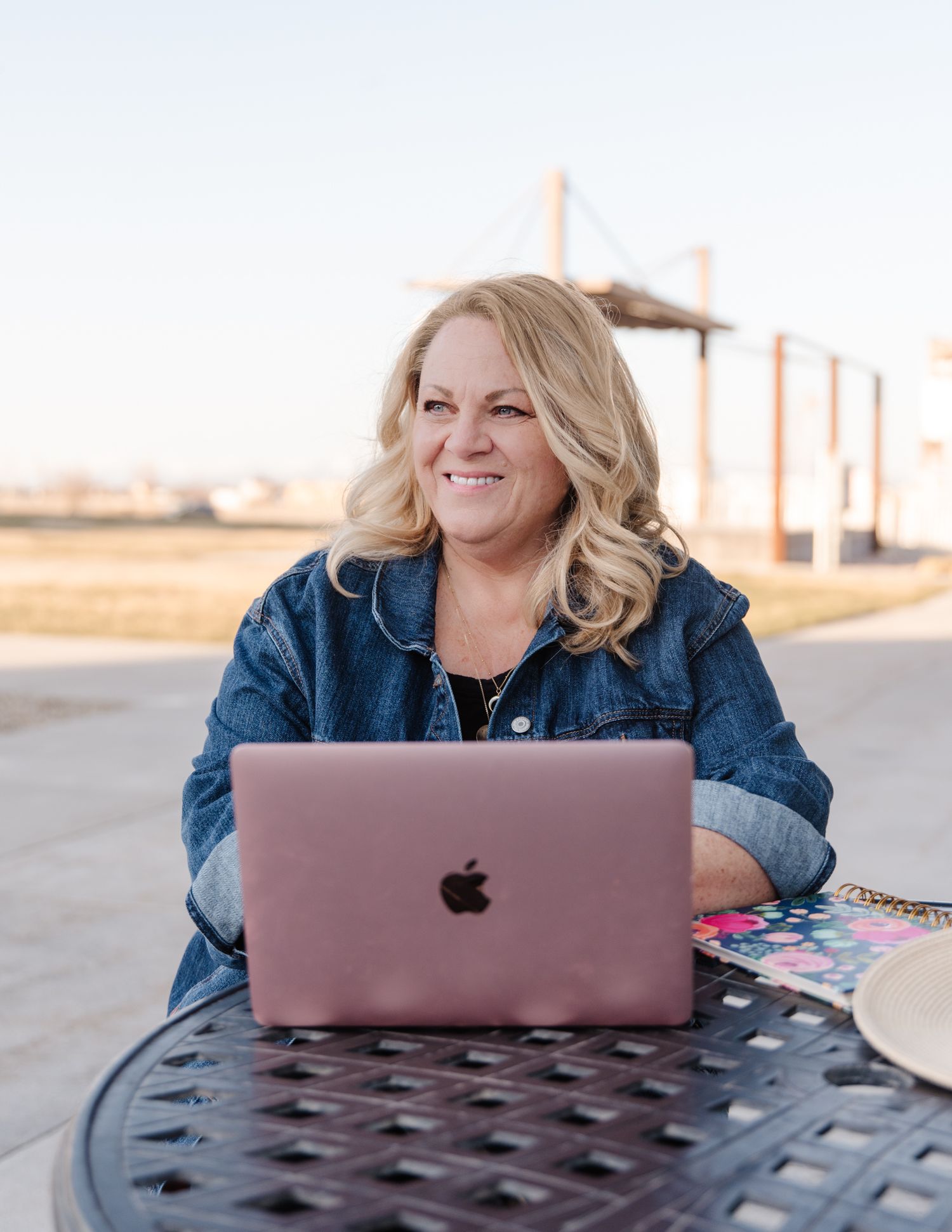 Professional working outdoors on a rose gold MacBook laptop at a patio table.