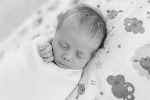 A sleeping newborn baby rests on floral patterned bedding in a black and white photograph.