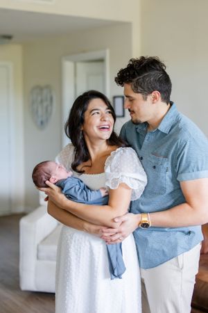 A couple shares a tender moment at home while holding their newborn baby dressed in blue.