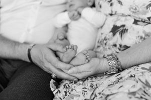 Black and white photo of tiny baby feet being gently cradled in an adult's hands against a floral fabric.