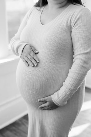 Black and white close-up of an expecting mother wearing a ribbed sweater while cradling her pregnant belly.