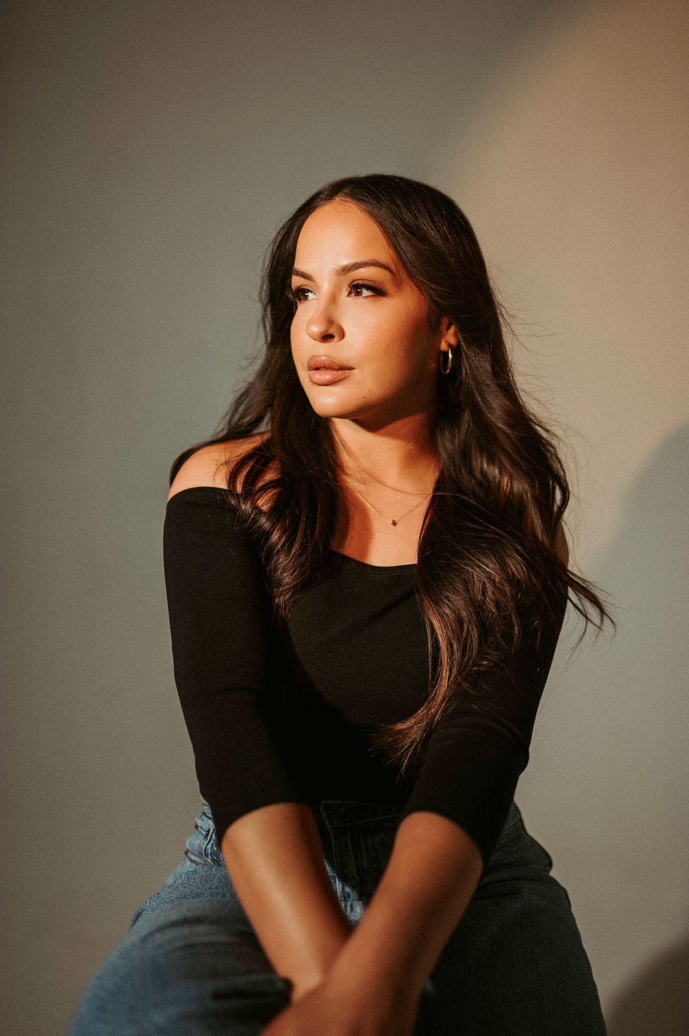 Artistic portrait series of a woman in black top and jeans against neutral background with moody lighting.