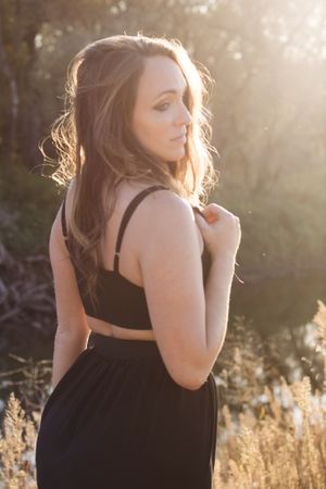 A person in black attire poses in golden hour sunlight among tall grasses.