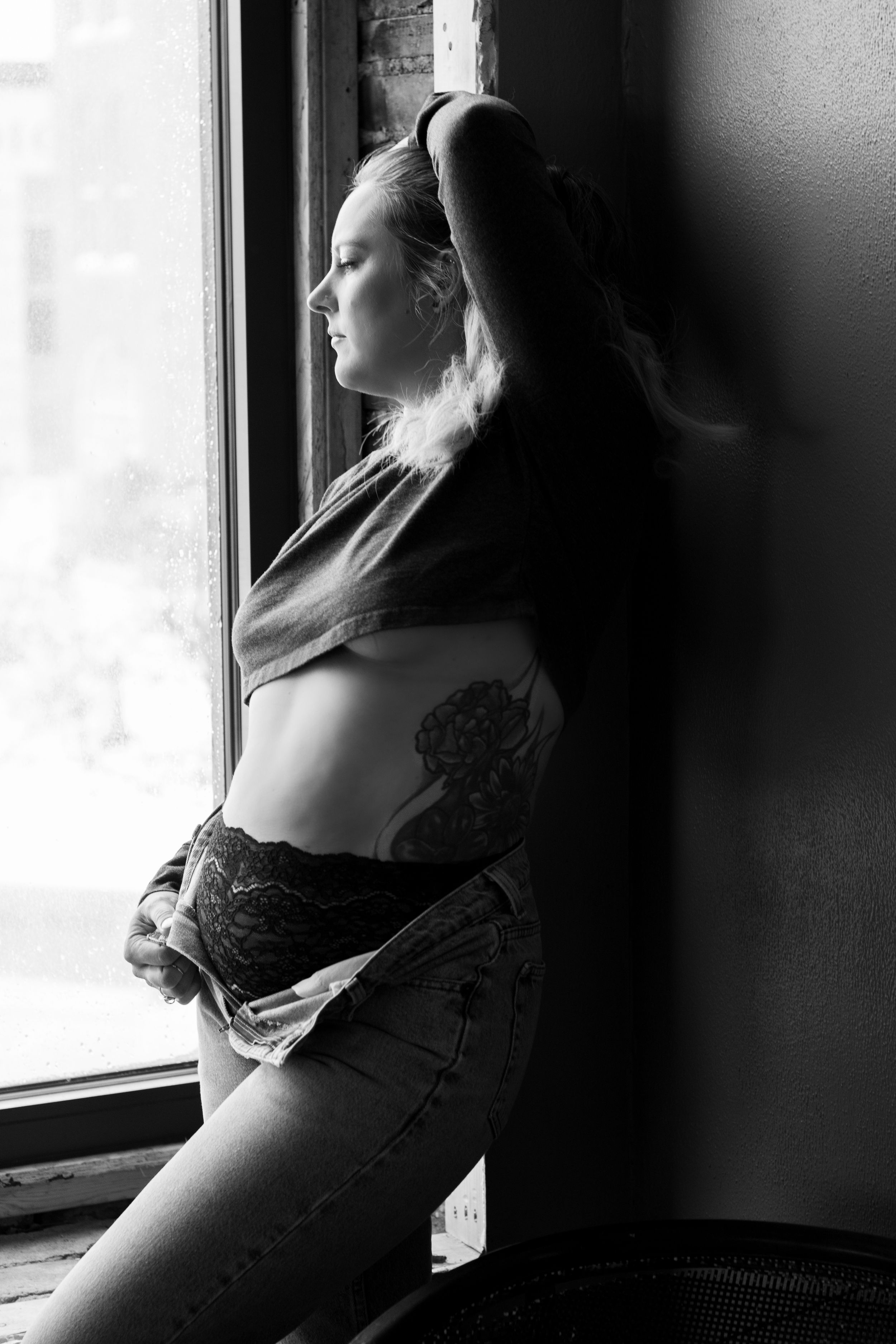 Black and white portrait by window showing tattoo and natural lighting.
