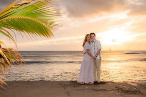 Couple in front of sunset in Hawaii with palm tree on left