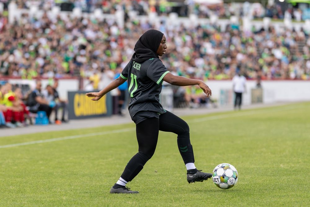 Soccer player in black uniform kicking a ball during an intense match.