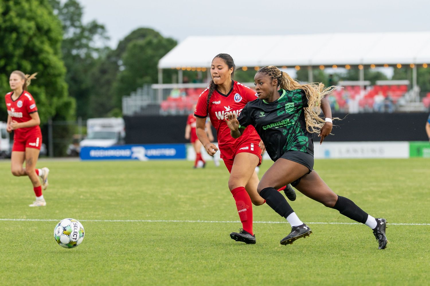 Soccer players in red and green uniforms competing for ball control on grass field.