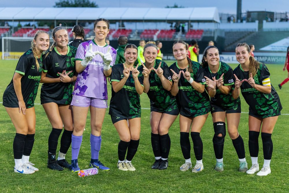 Women's soccer team lined up on field wearing dark uniforms.