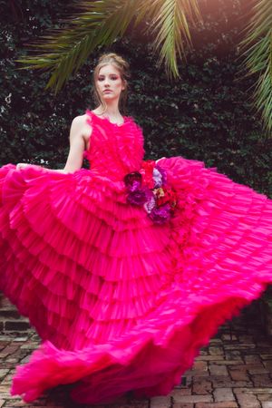 A vibrant hot pink ruffled couture gown with layers of tulle fabric twirls dramatically on a brick patio near tropical foliage in New Orlean
