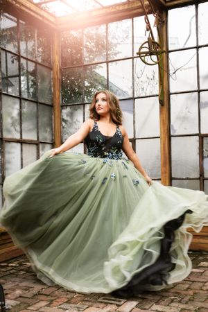Flowing sage green couture gown twirls dramatically in a sunlit greenhouse setting in New Orleans.