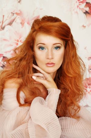 Beautiful portrait of a girl with flowing red hair against pink floral background wearing a couture gown.