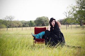 A photograph showing a person sitting in a antique theatre seat in a grassy meadow on a sunny day.