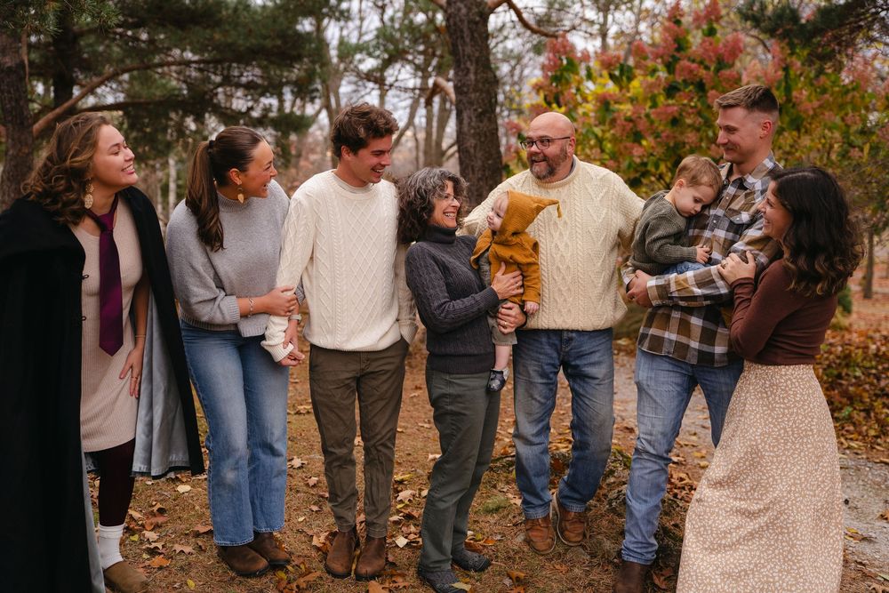 Group of people gathered outdoors in autumn setting with colorful fall foliage in background.