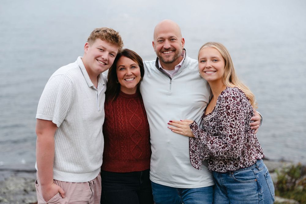 A family poses together outdoors near a waterfront on a cloudy day.