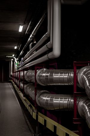 Metal ventilation ducts and pipes arranged in industrial corridor.