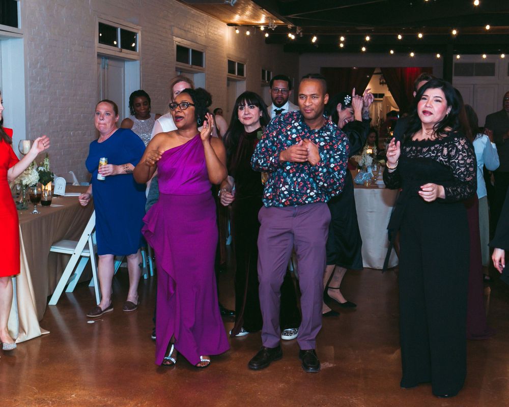 Wedding guests dancing in a reception hall decorated with string lights.