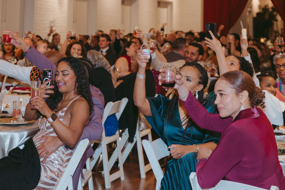 Wedding guests cheer and raise their hands enthusiastically during a celebration in an indoor venue.