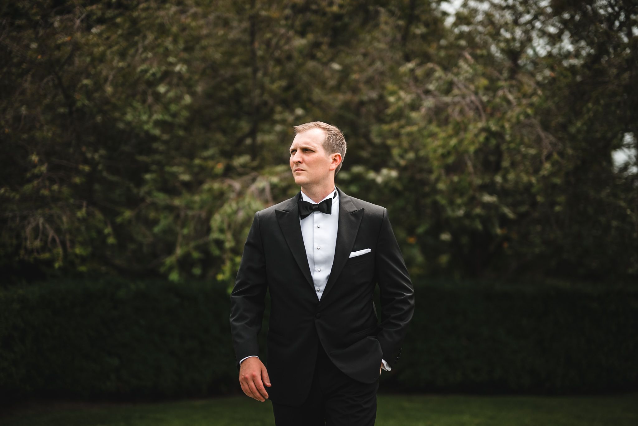 editorial style groom portrait where he looks off the the camera left with greenery as a backdrop