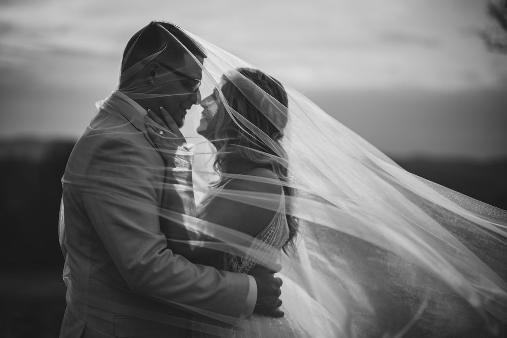 A flowing white wedding veil billows in the wind against a dramatic black and white sky at the garrison