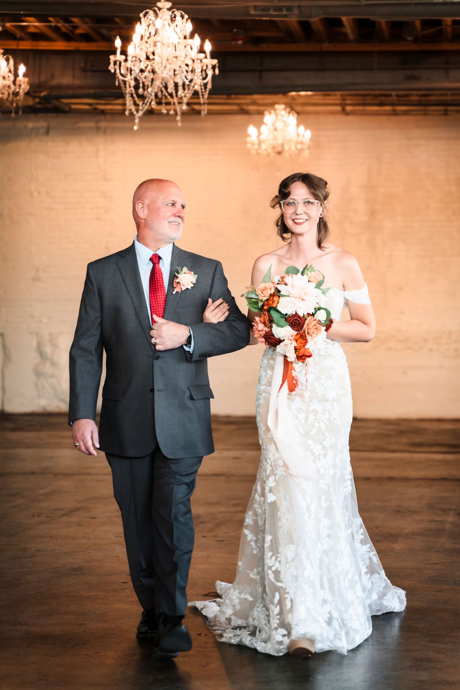 Elegant wedding scene with two people walking arm in arm under crystal chandeliers in an indoor venue.