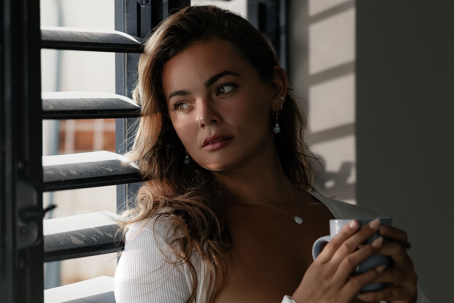 Moody portrait of someone in white by a window with natural light and shadows.