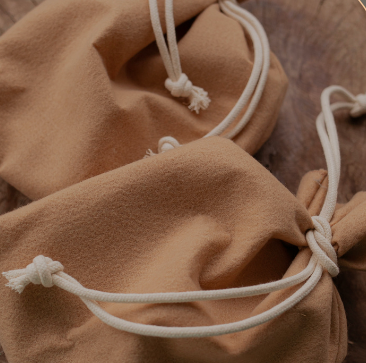 Close-up of tan suede drawstring pouches with white cord ties resting on a wooden surface.