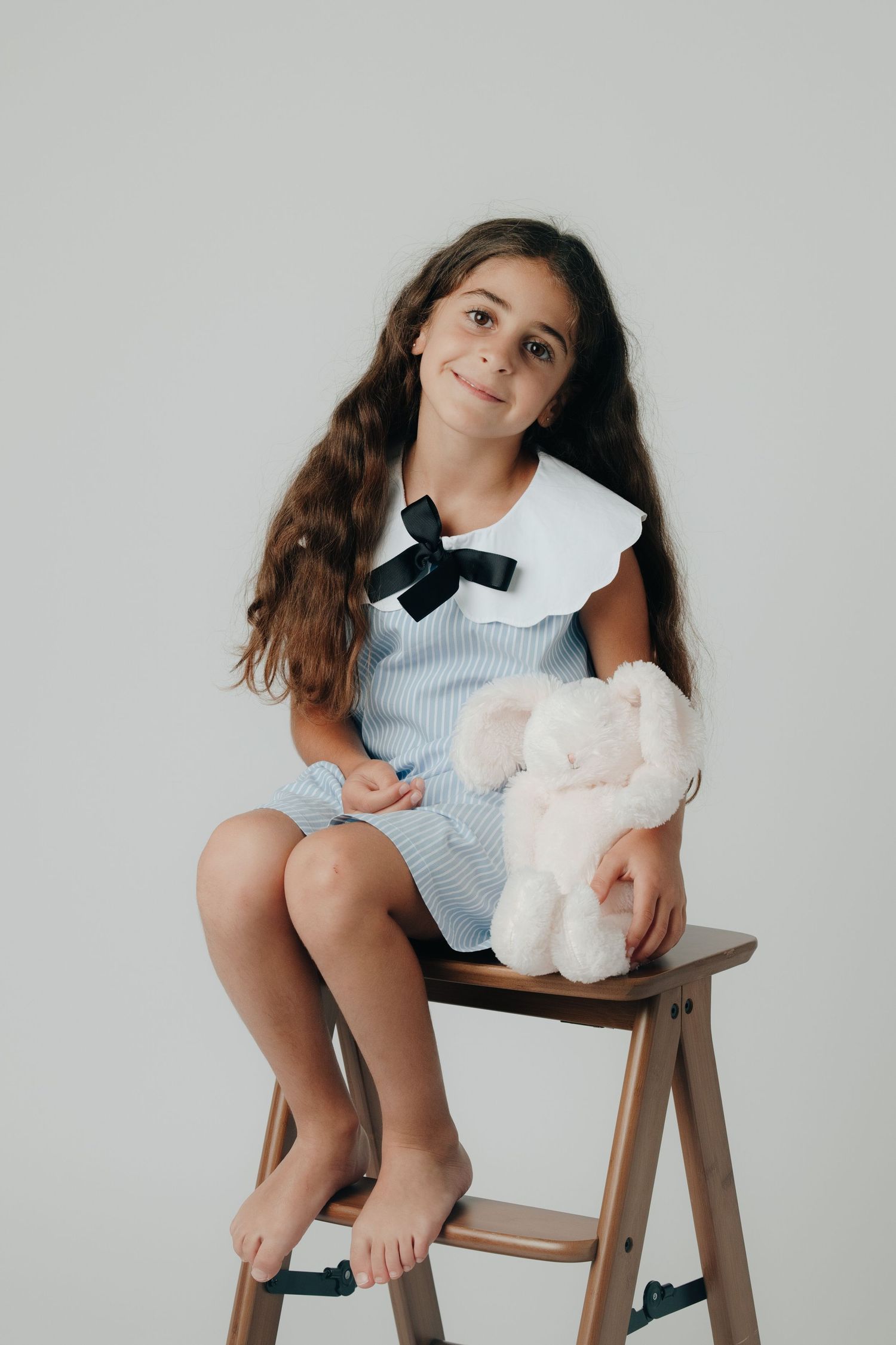 Two young girls in white outfits pose with stuffed animals and a cactus toy on a white rocking chair.