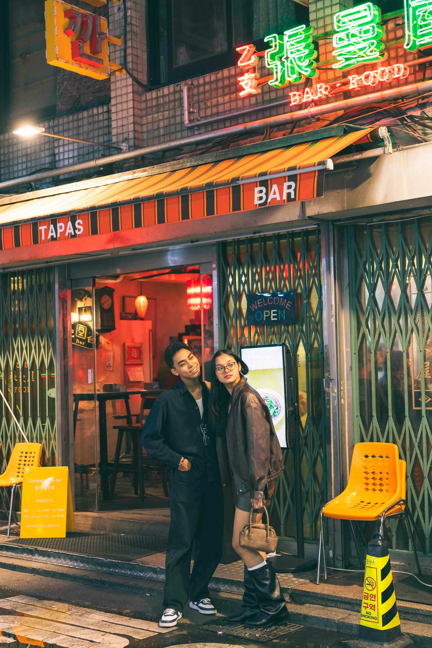 Couple posing outside a neon-lit tapas bar and restaurant at night in Asia.