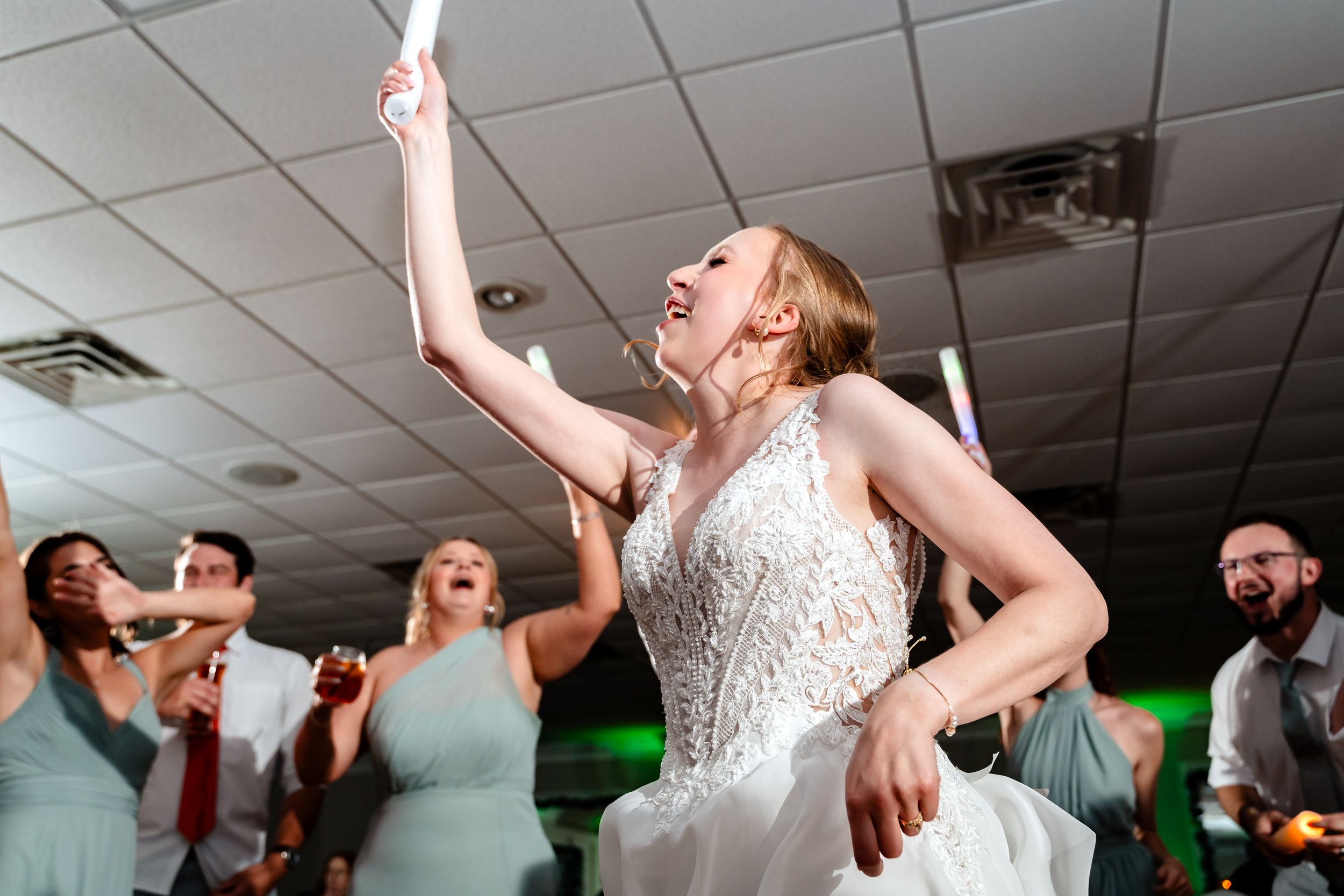 An excited bride in a lace gown dances energetically at her wedding reception.