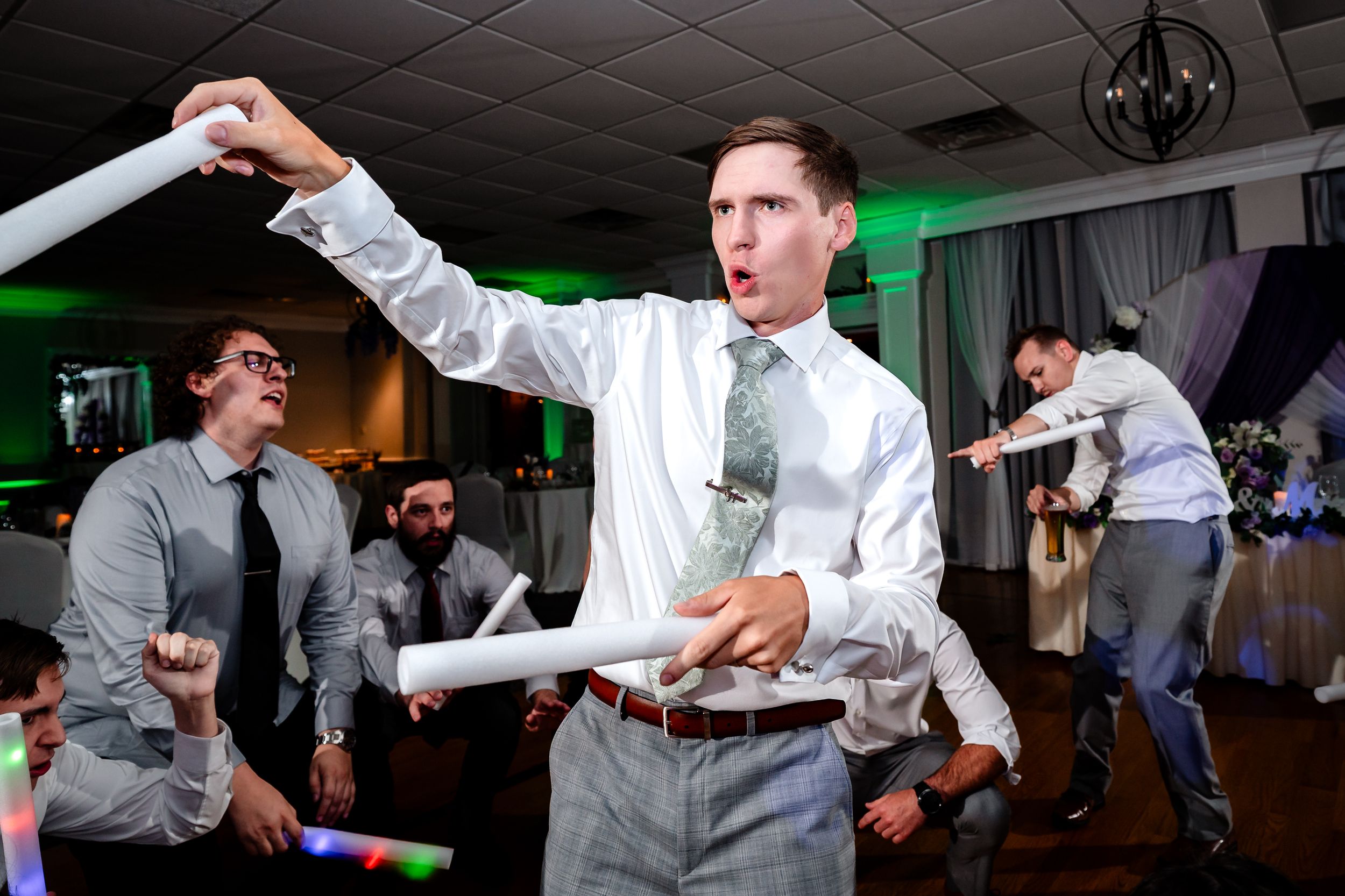 Energetic wedding guest waves glow stick on dance floor during lively reception party.