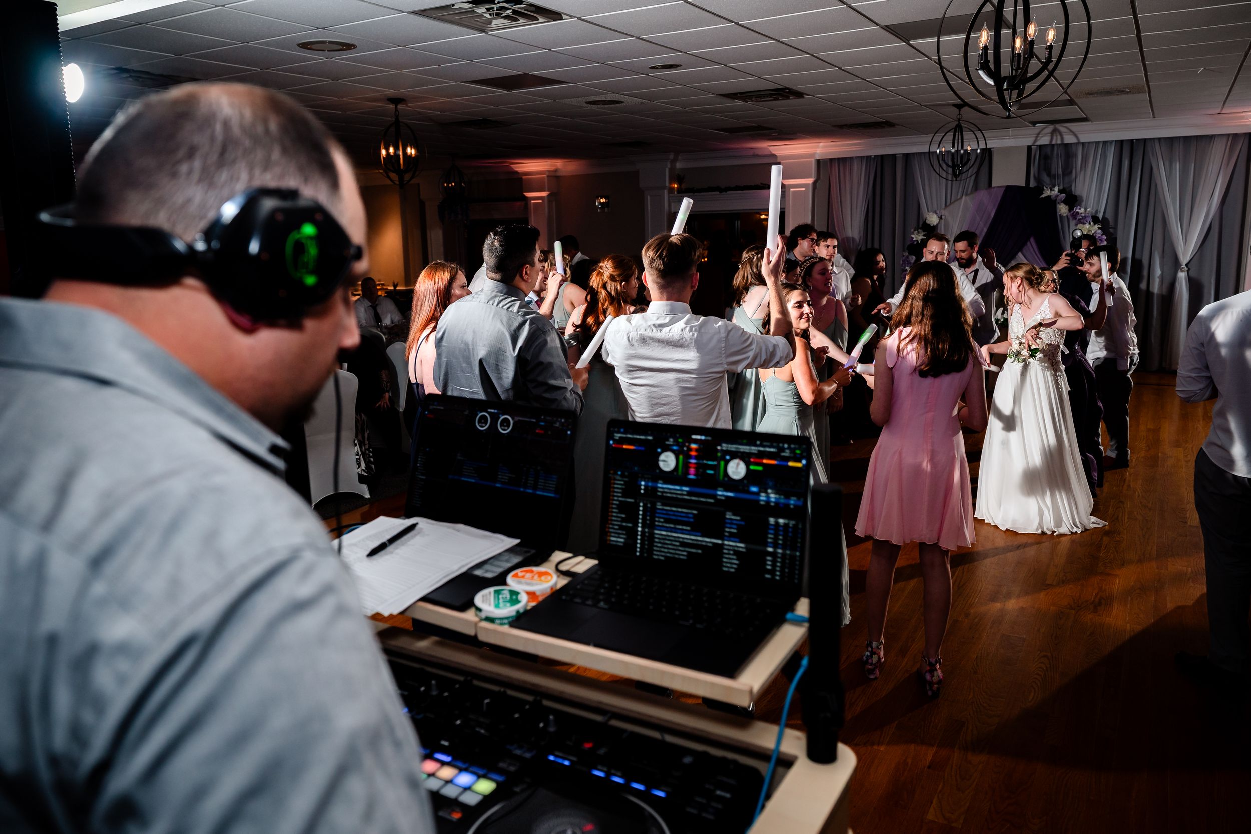 DJ controls music while wedding guests fill the dance floor at a lively reception.
