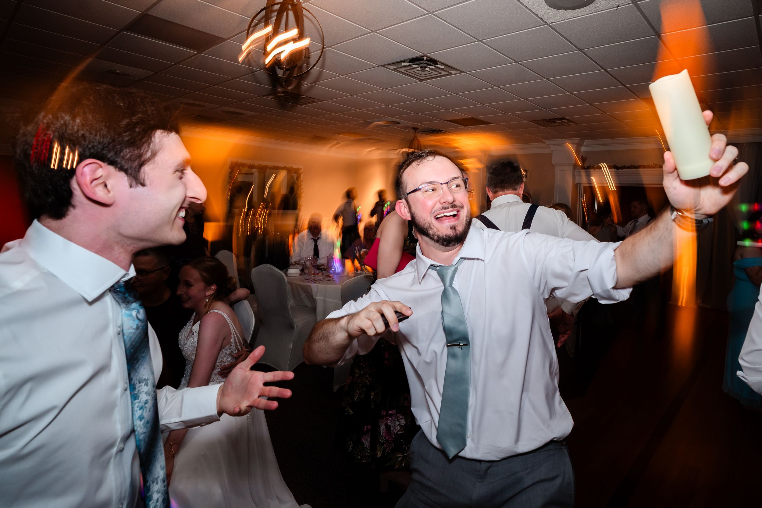 Wedding guests dancing and celebrating with glow sticks during energetic indoor wedding reception party.