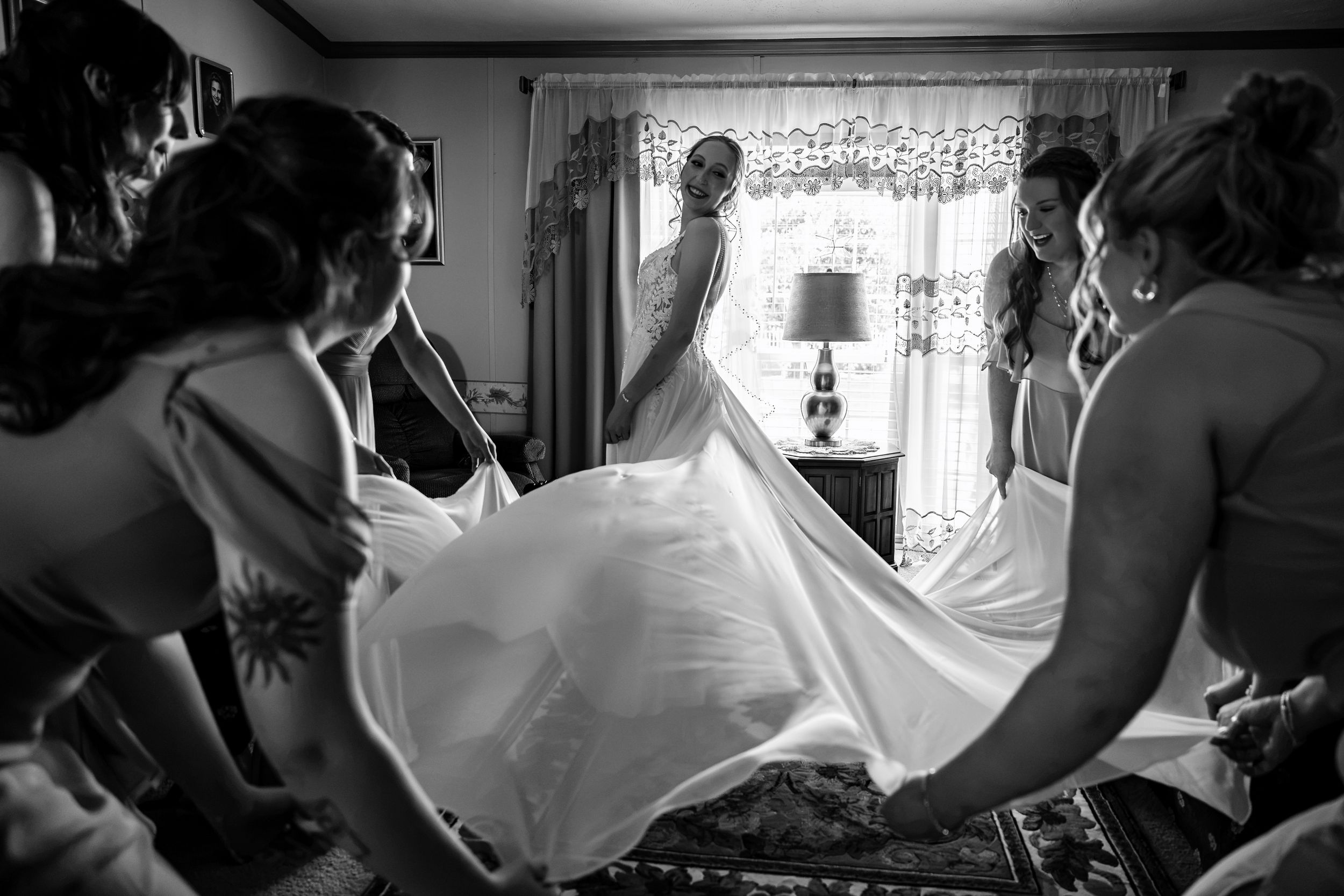 Black and white photo of bridesmaids helping bride into her wedding gown before ceremony.