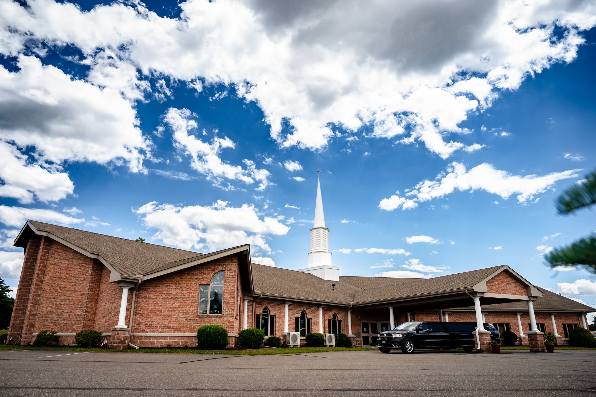 A brick church with a white steeple stands under a dramatic blue sky with fluffy white clouds.