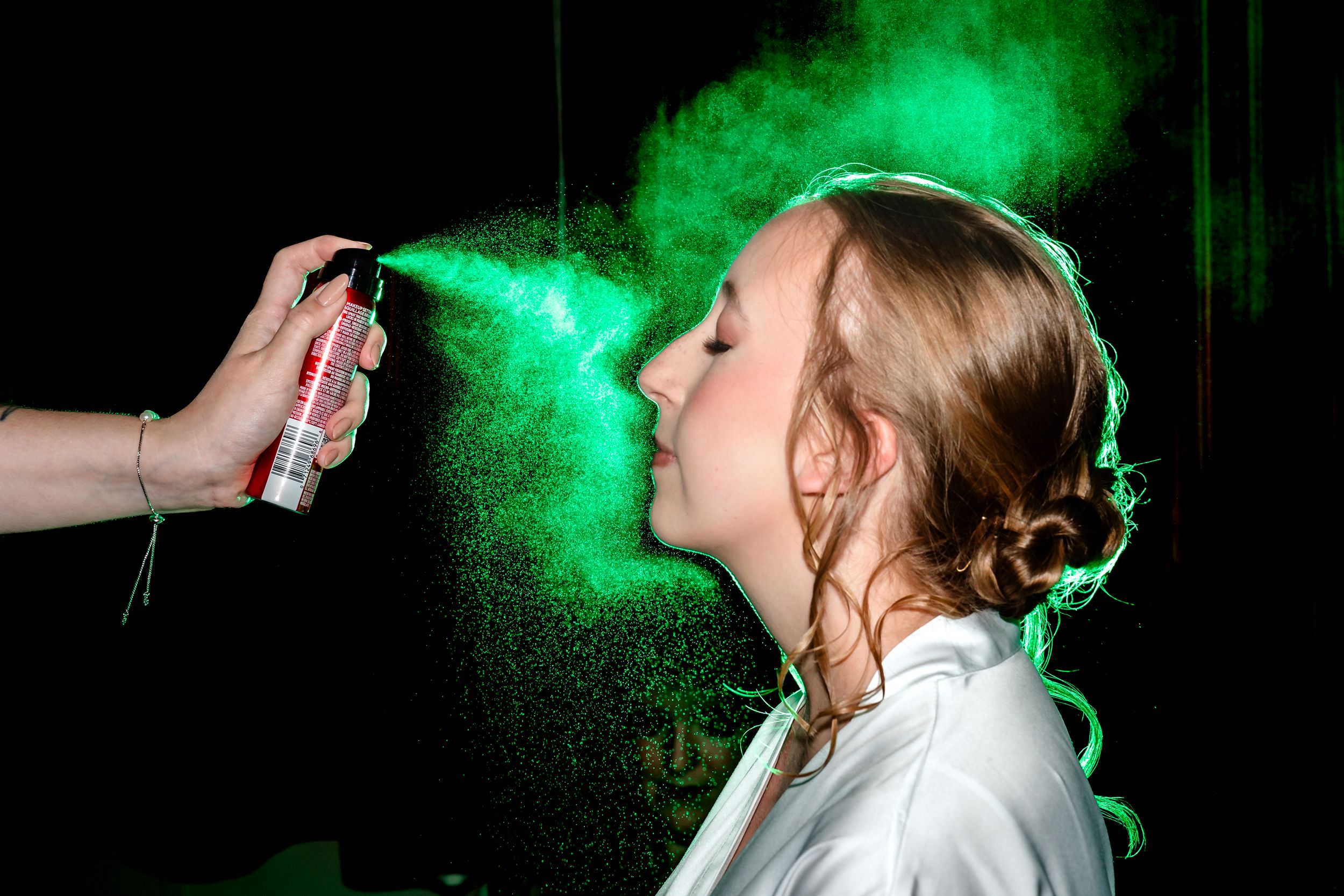 Green hair spray mist being applied to a blonde bride during wedding preparation.