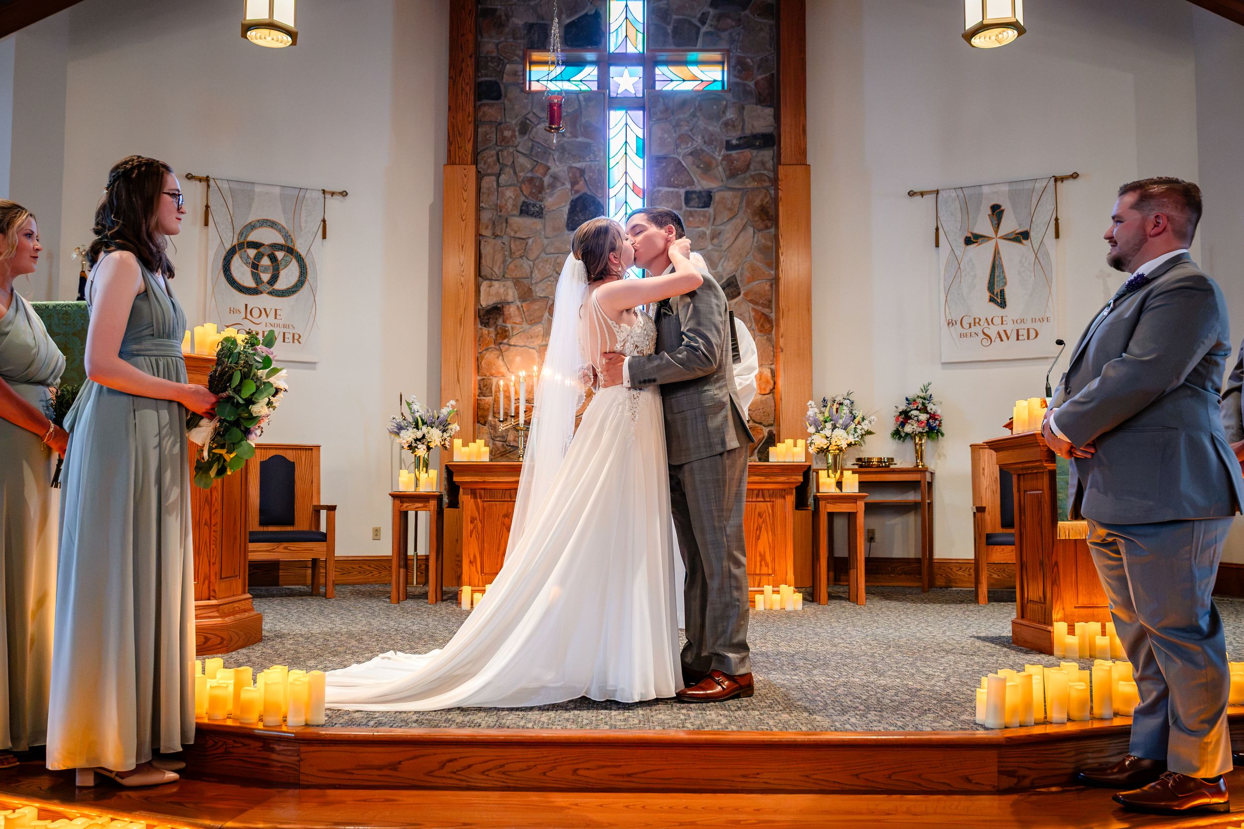 Bride and groom share first kiss at church altar surrounded by candles and guests.
