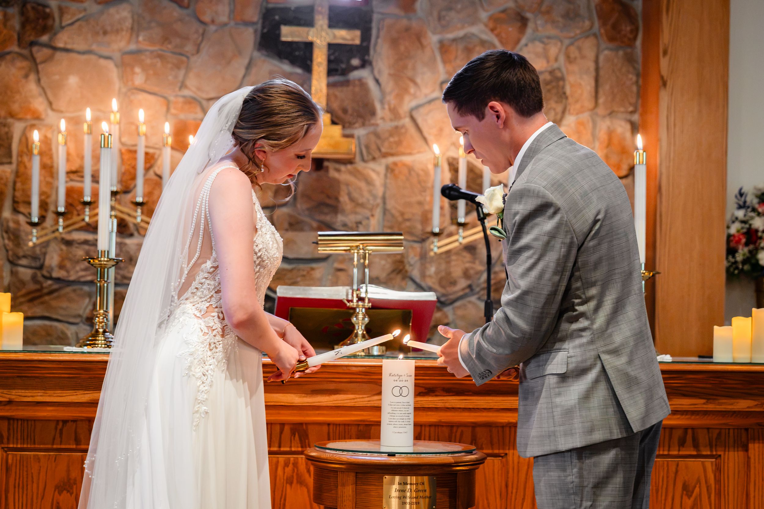 Bride and groom light a unity candle together at the altar during wedding ceremony.