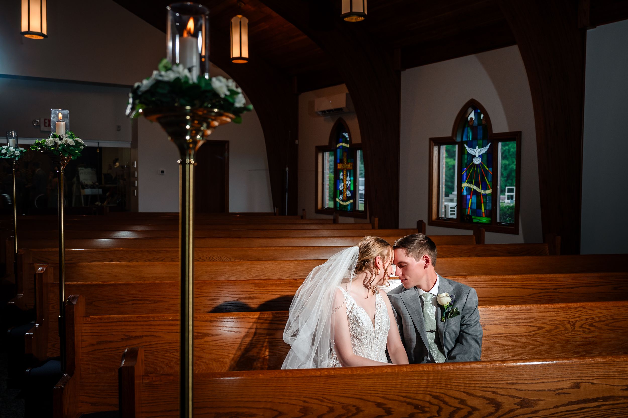 Bride and groom share an intimate moment kneeling together in a candlelit church.