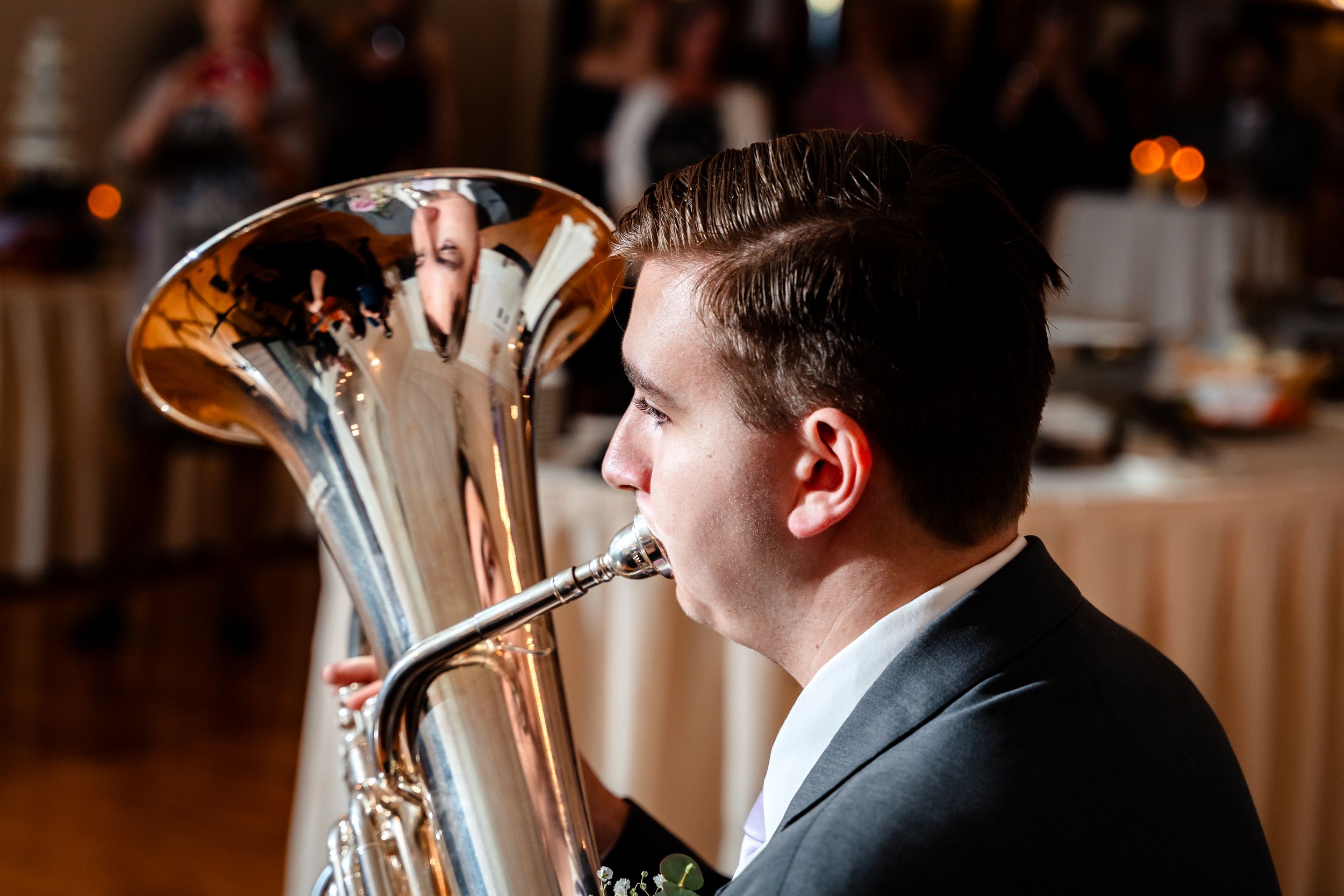 A young man in a suit plays a shiny tuba at an elegant wedding reception.