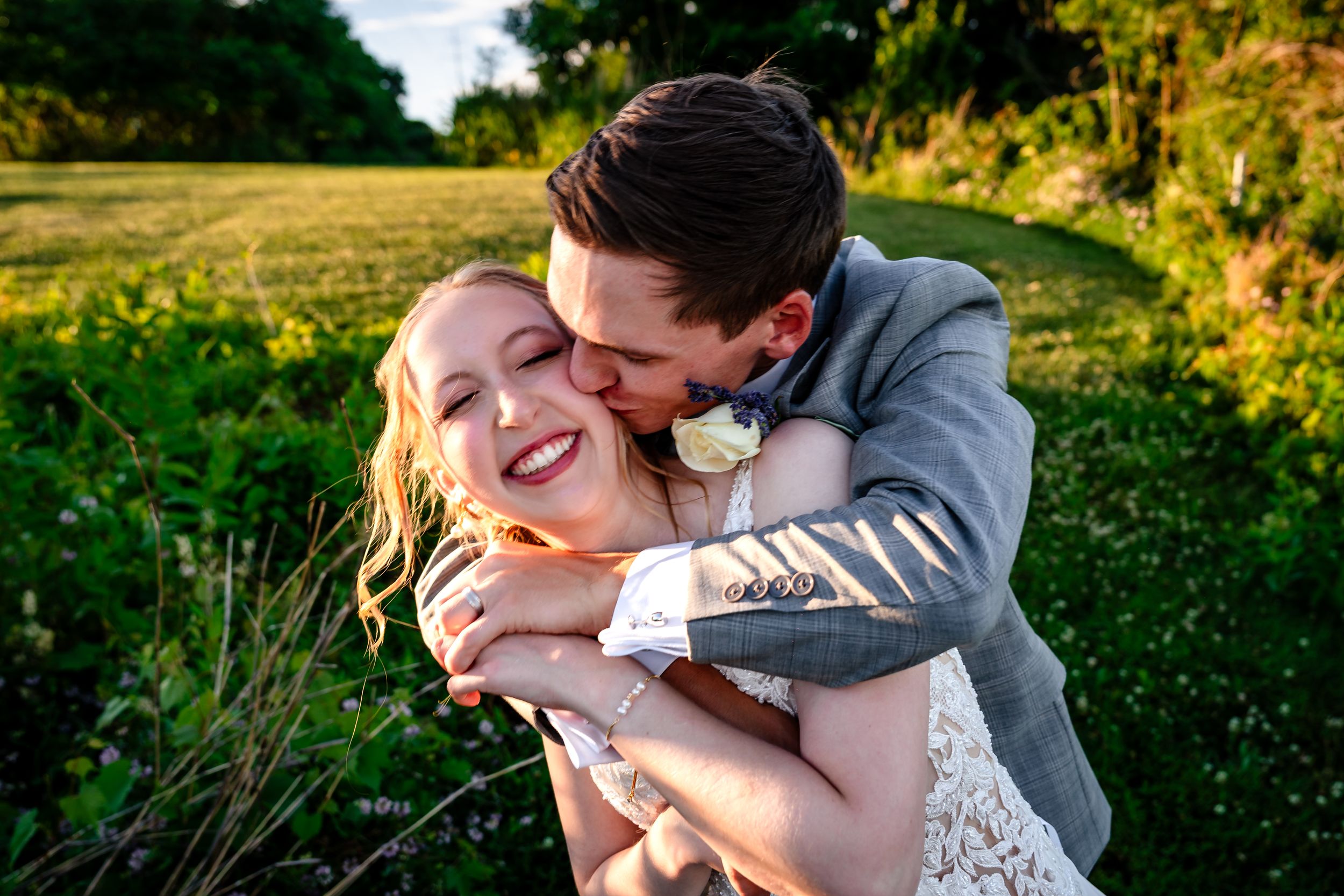 Bride and groom share a joyful embrace outdoors in golden hour light during their wedding day.