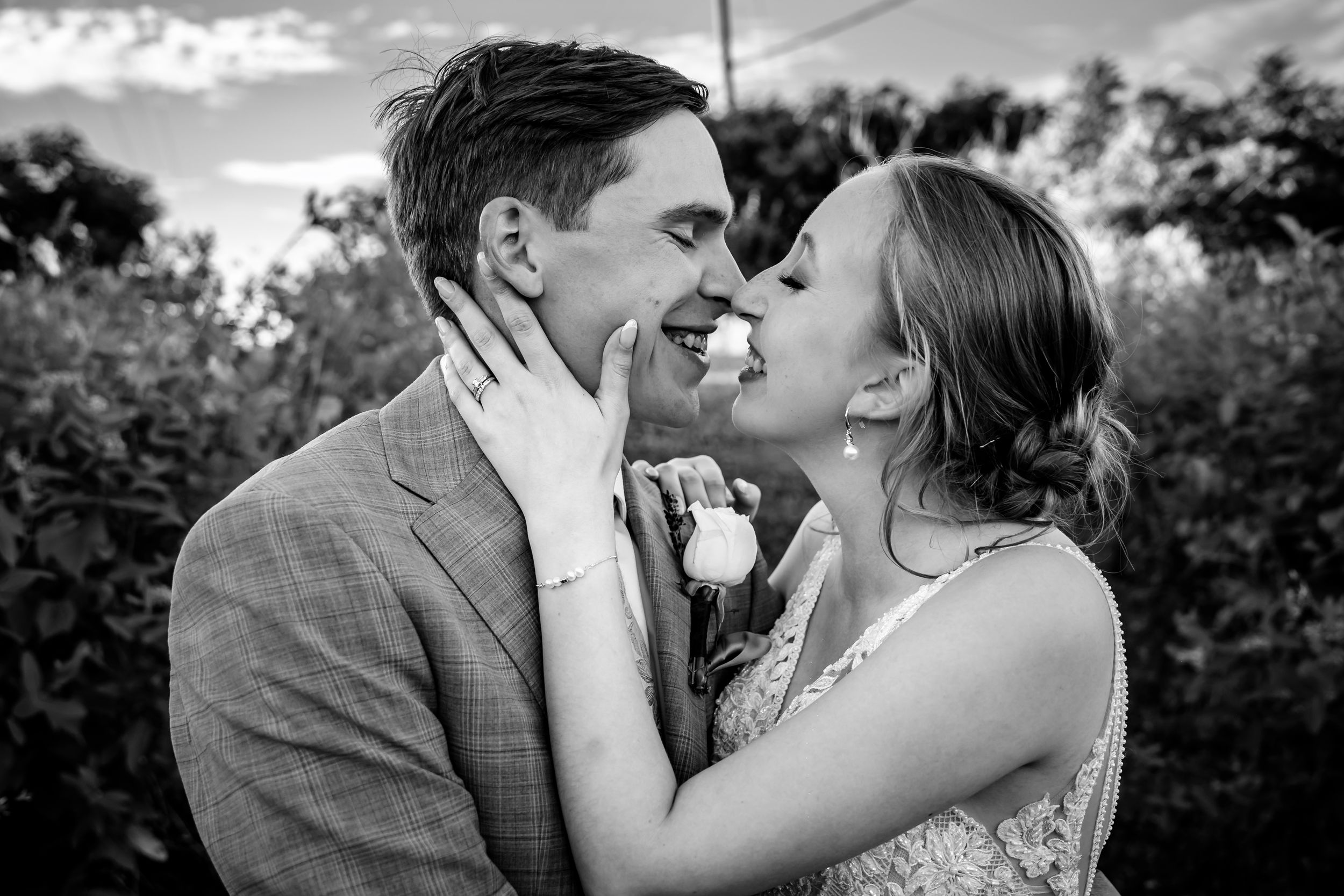 Black and white photo of bride and groom sharing an intimate moment, almost kissing outdoors.