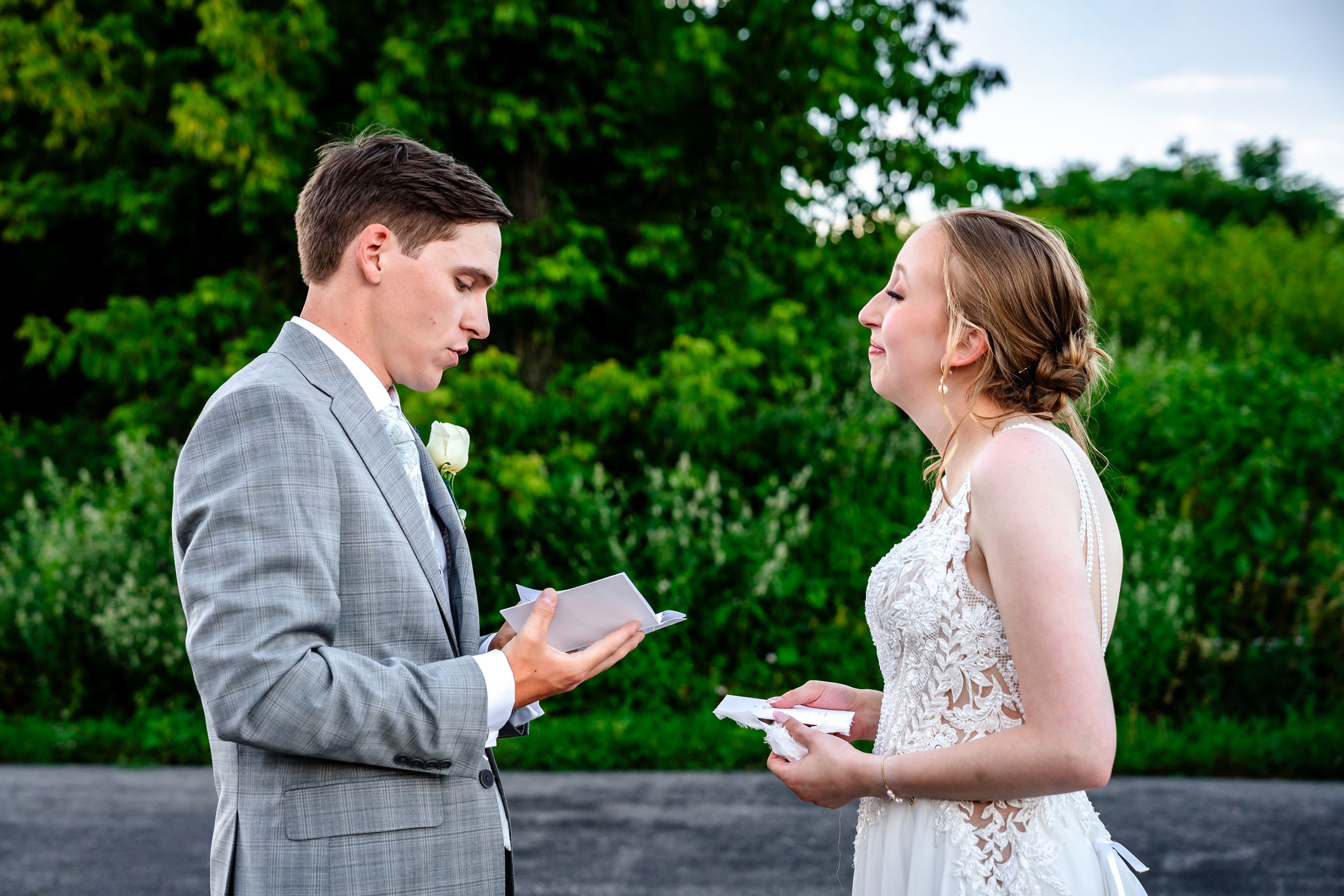 Bride and groom exchange personal vows outdoors, each holding handwritten notes during their wedding ceremony.