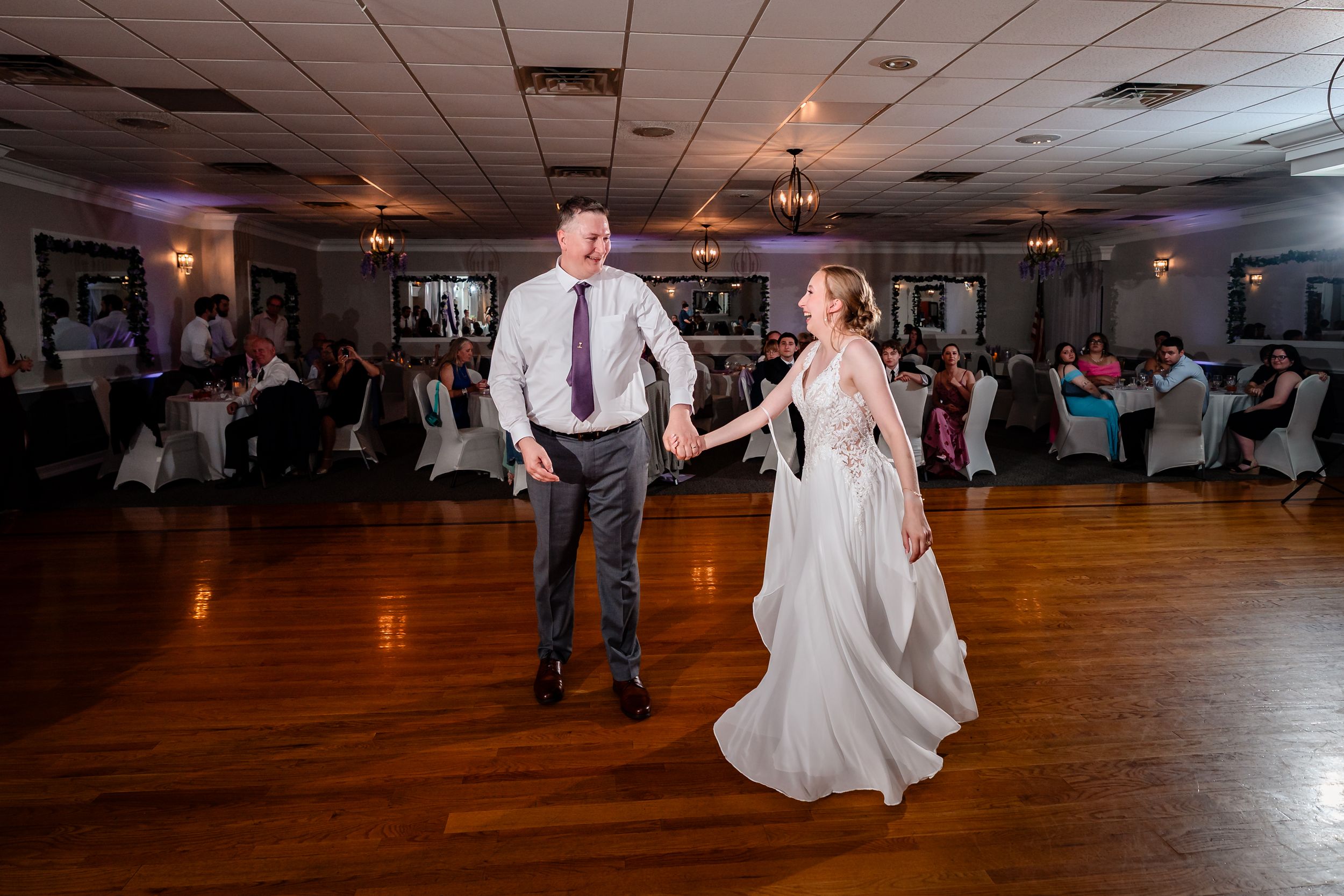 Bride and groom share first dance on wooden ballroom floor at elegant wedding reception.