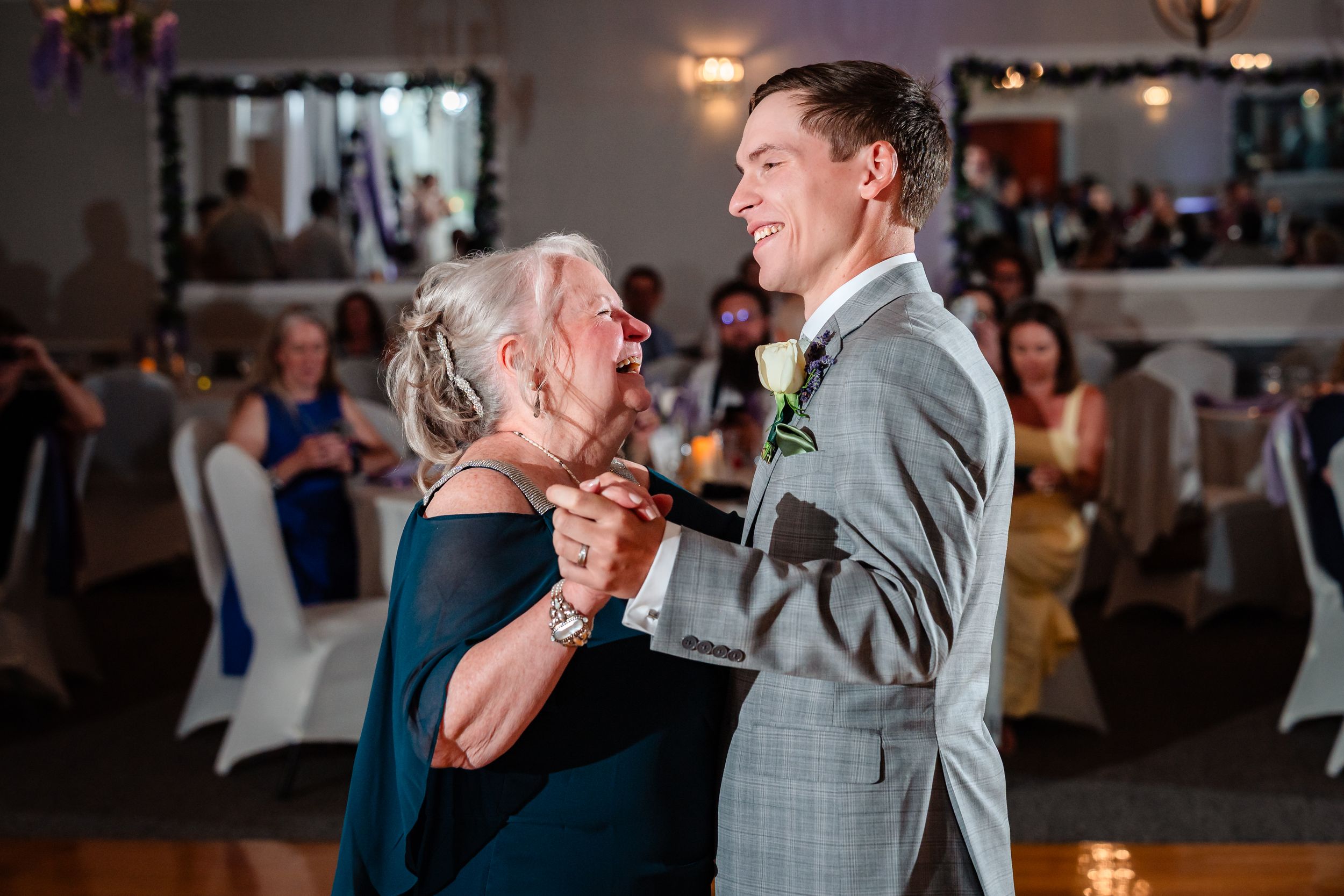 Groom in gray suit shares a tender mother-son dance at elegant wedding reception.