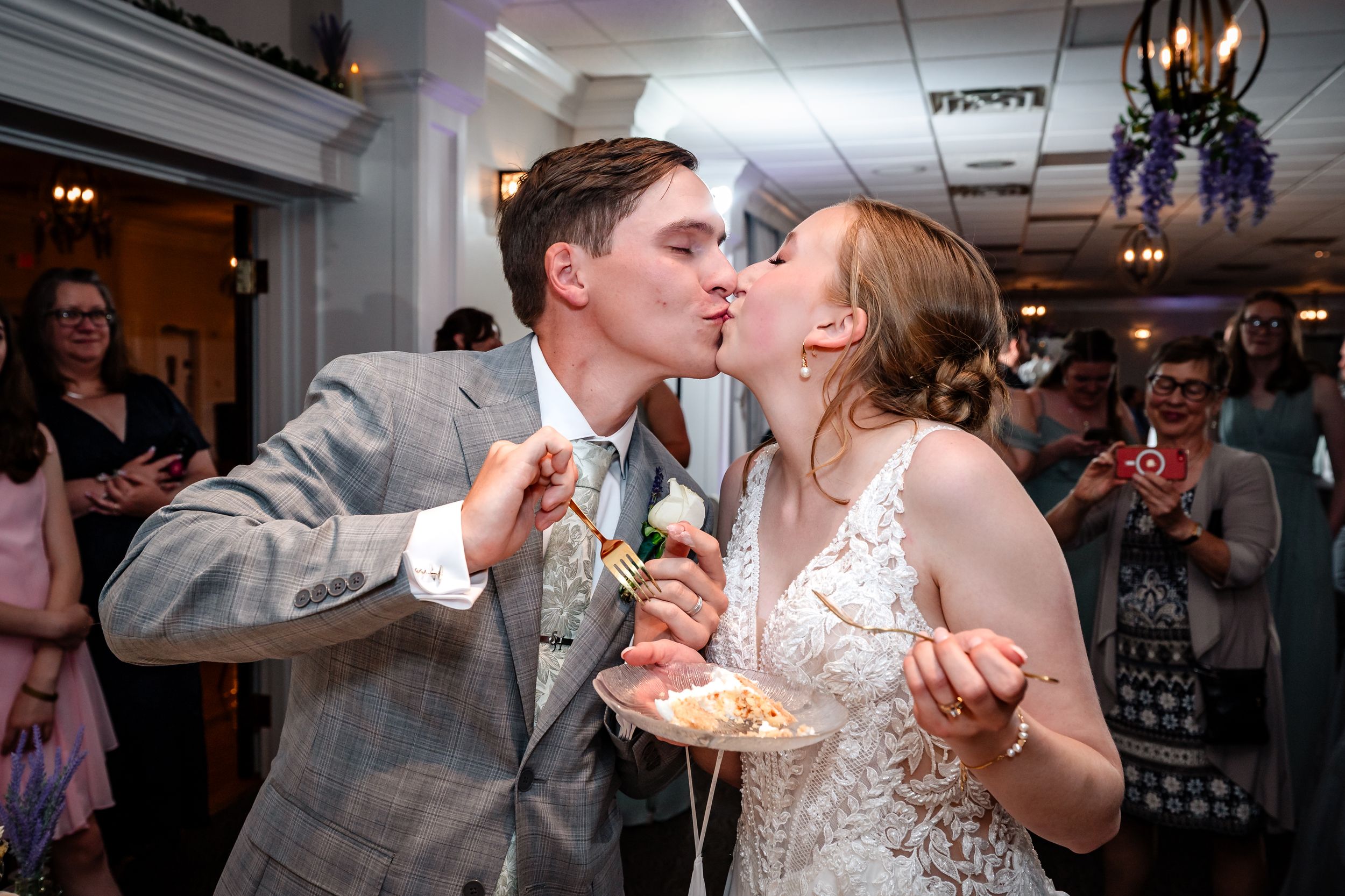Bride and groom share a kiss while eating wedding cake at their reception.